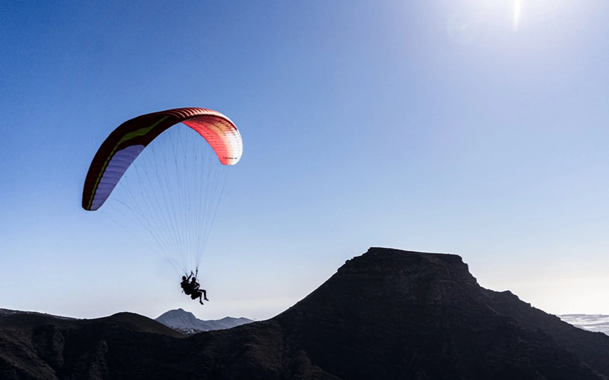 A tandem paragliding wing in silhouette above a dark volcanic summit