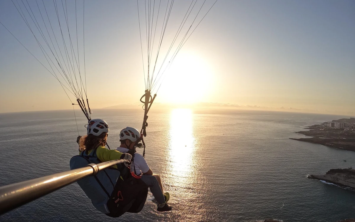 Um par de parapente em tandem a voar em direção a um sol baixo sobre o Atlântico ao largo de Costa Adeje