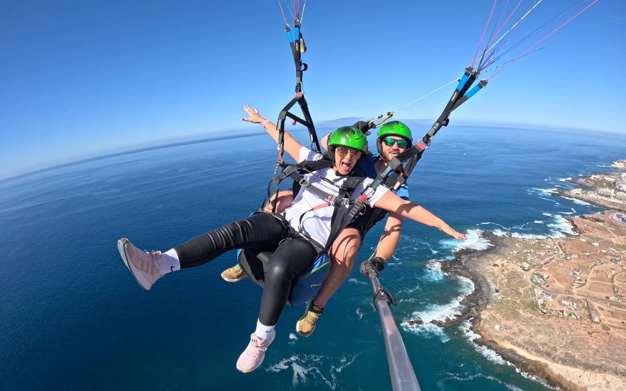 Um passageiro com capacete verde e braços abertos sobre água azul-escura e uma ponta rochosa baixa