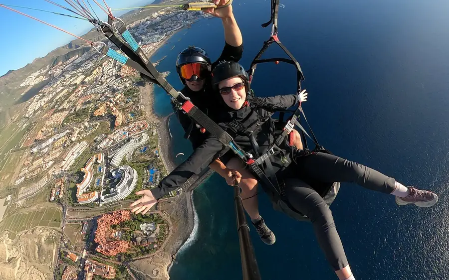 Um par tandem a inclinar-se sobre as torres dos resorts e a costa de areia escura de Costa Adeje