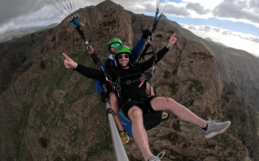 Dois pilotos a apontar para a câmara em frente a um alto cume rochoso bem acima do vale