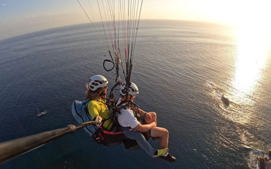 Um piloto e um passageiro lado a lado sobre água aberta, o sol baixo a deixar um rasto dourado no mar