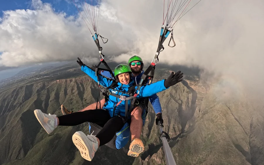 Um par tandem de azul a voar junto às nuvens, com uma longa crista montanhosa escura por baixo