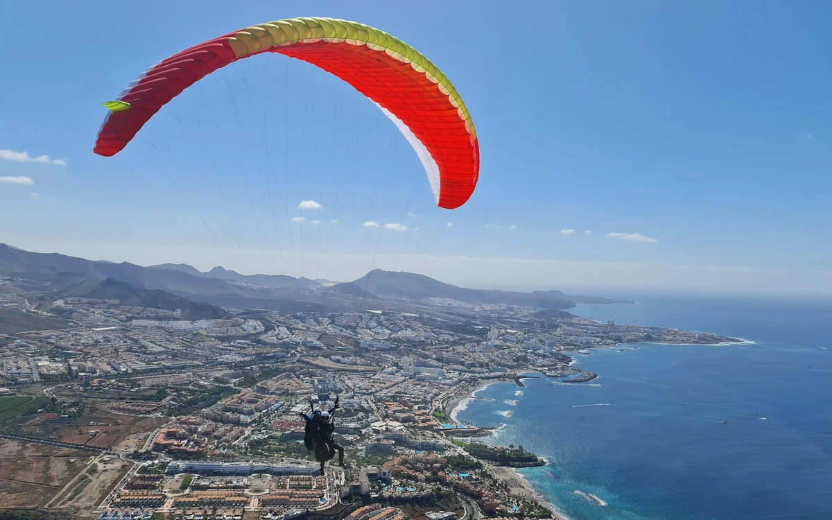 Uma asa de parapente vermelha sobre a costa urbanizada de Costa Adeje, com promontórios a estender-se para norte