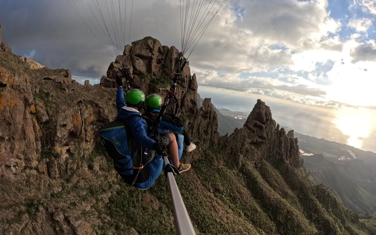 Duas pessoas num arnês de parapente tandem pouco acima de uma crista rochosa íngreme no sul de Tenerife