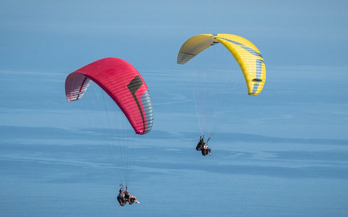 Duas asas de parapente, uma rosa e uma amarela, a voar contra o mar azul liso